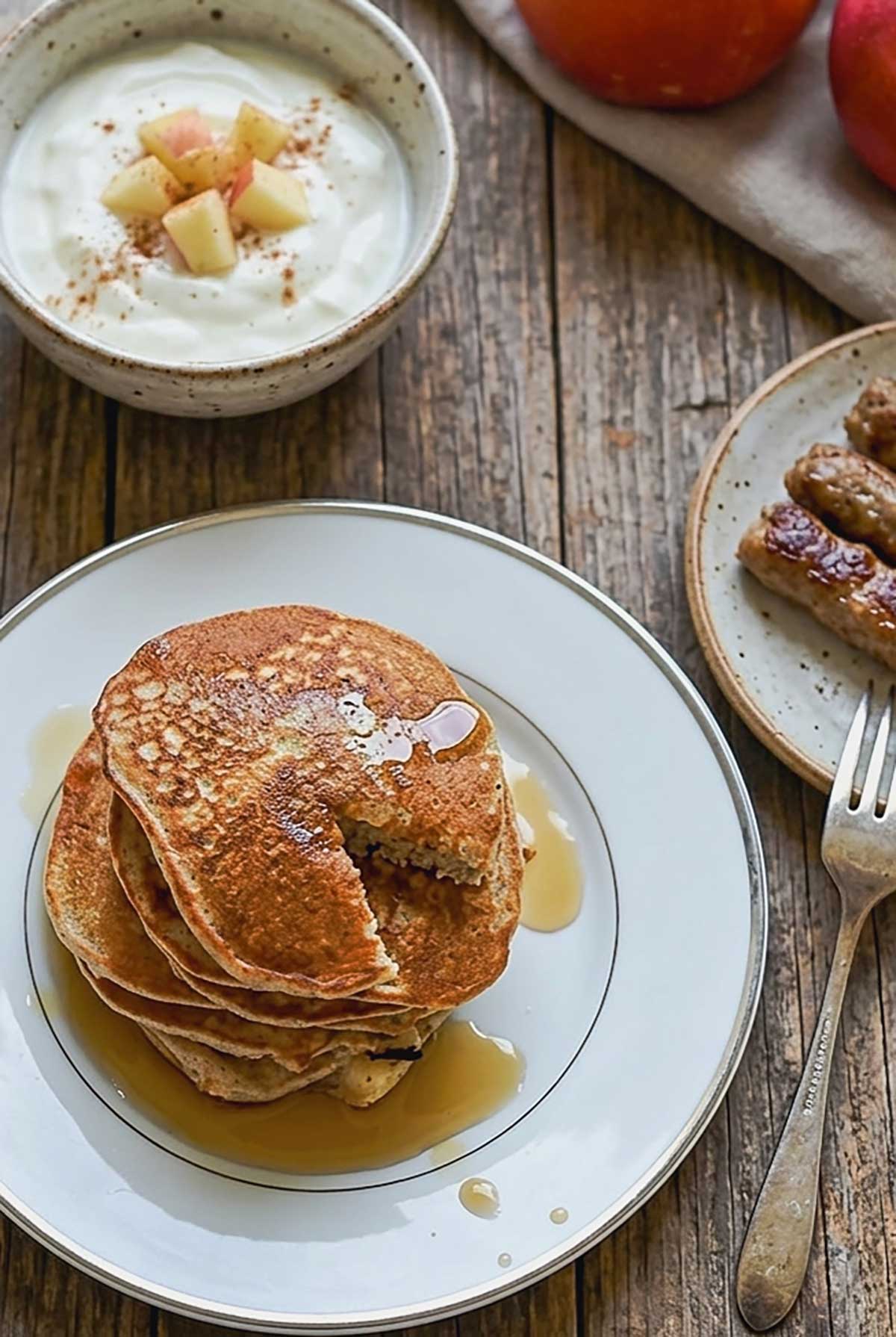 stacked apple cinnamon buckwheat pancakes with a piece missing drizlzed with maple syrup and a side of df yogurt