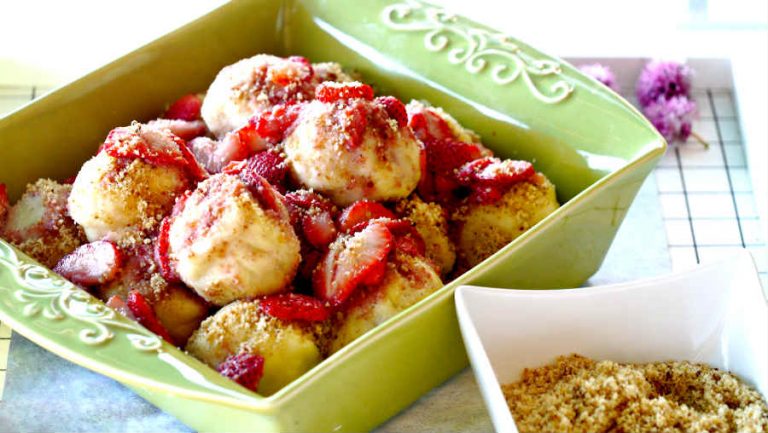 Gluten-free Strawberry dumplings in a green serving dish topped with sliced strawberries and a nut-sugar crumble.