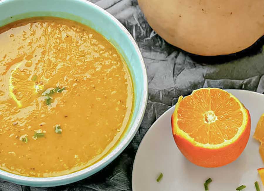 butternut squash bisque in a bowl with half an orange on a plate