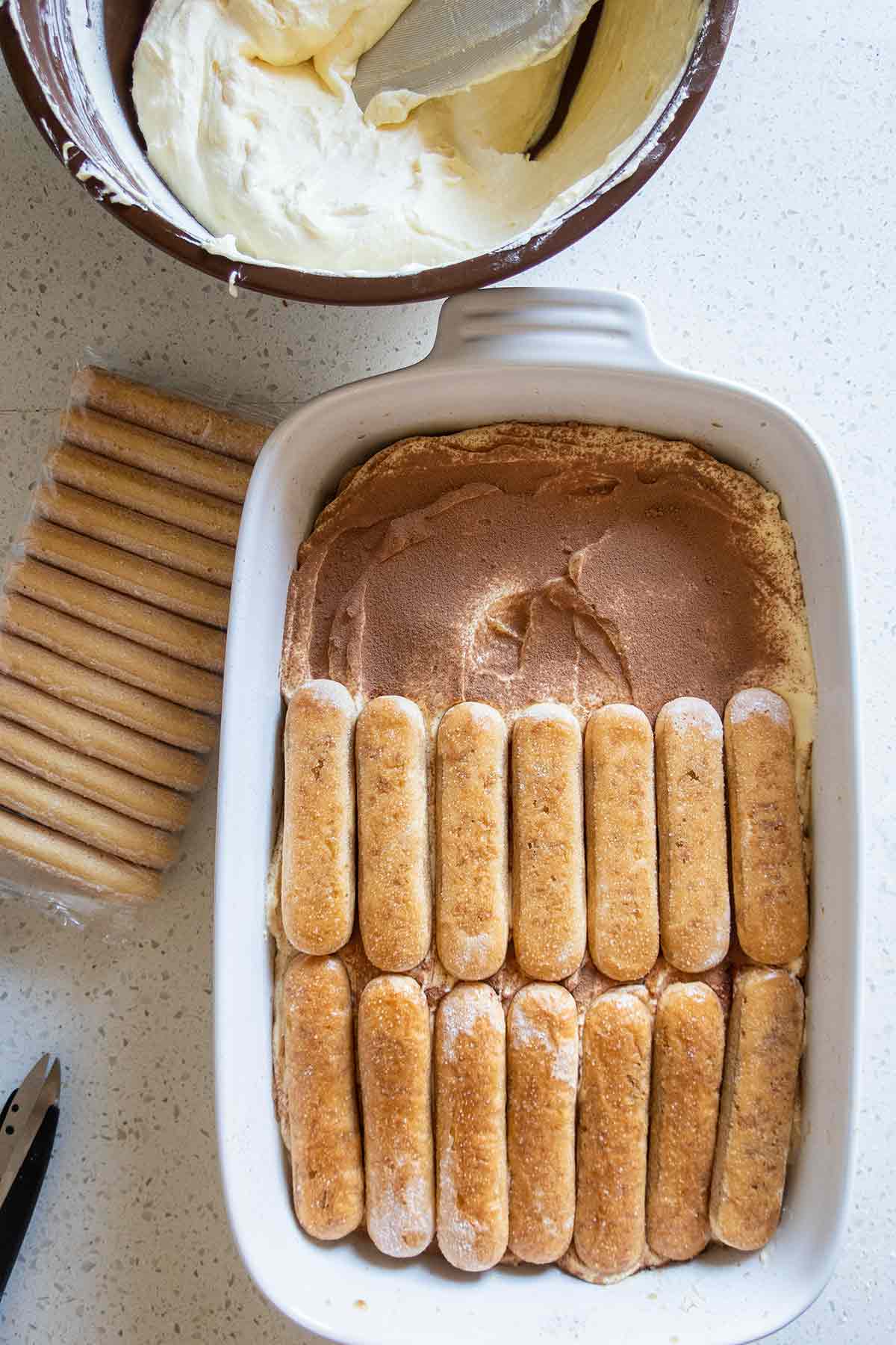 showing layers of tiramisu with lady fingers and cream layers in a dish