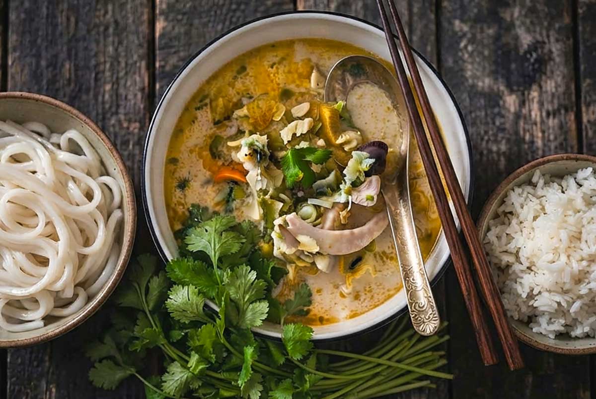 Bowl of Spicy Thai Coconut Chicken Soup with Vegetables and a side or rice and noodles