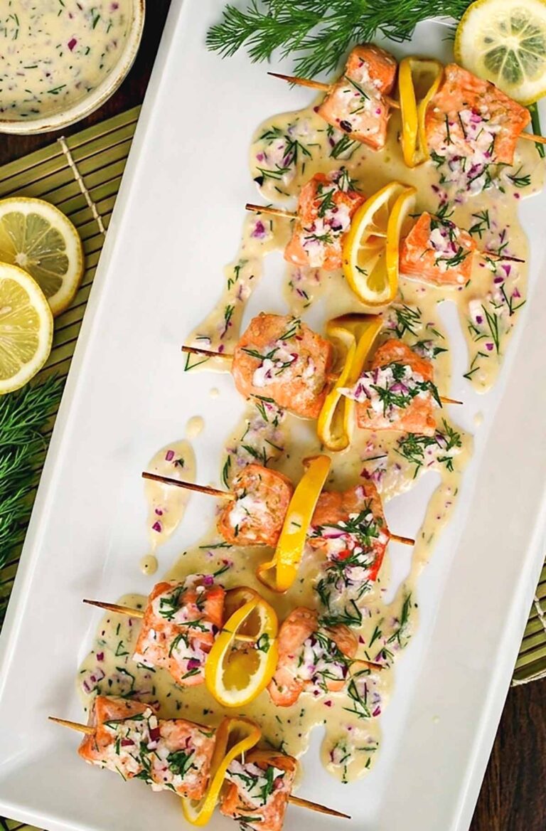 Salmon pops on skewers on a plate drizzles with piquant dill sauce and lemon slices