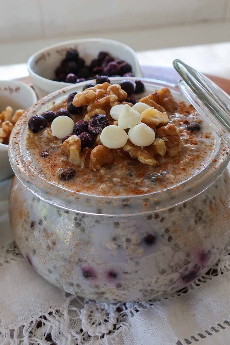 A glass jar filled with creamy gluten-free overnight oats mixed with chia seeds, ground flax, and topped with fresh berries, walnuts & white chocolate chips