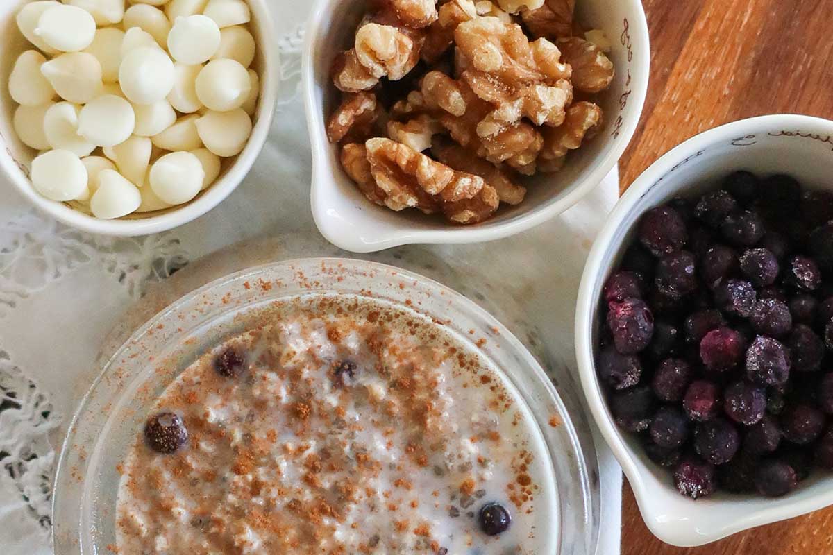A glass jar filled with creamy gluten-free overnight oats mixed with chia seeds, ground flax, and blueberries with side bowl of various toppings