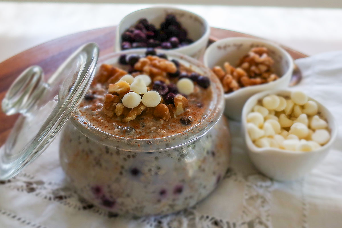 A glass jar filled with creamy gluten-free overnight oats mixed with chia seeds, ground flax, and topped with fresh berries, walnuts & white chocolate chips