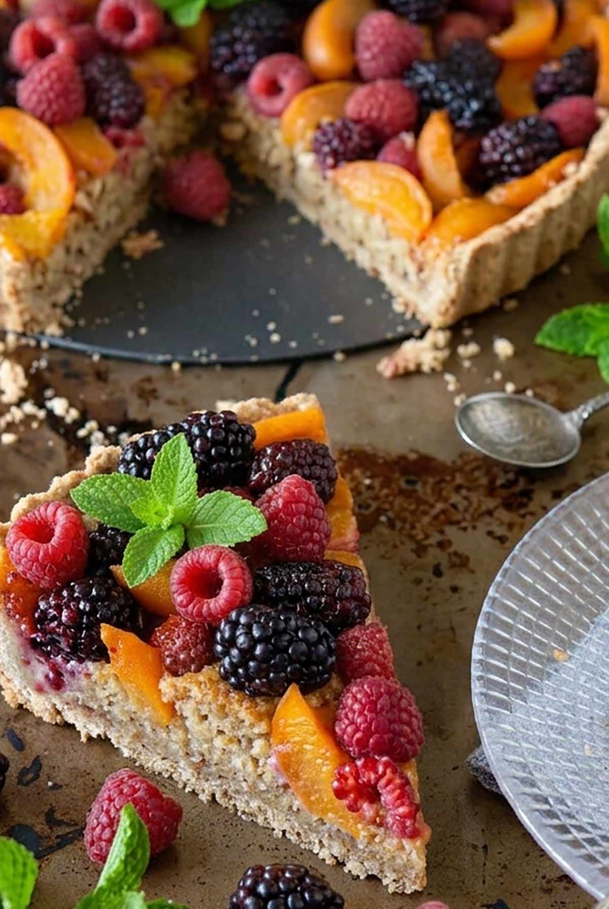 slice of fresh fruit tart, apricots, berries on an almond crust topped with mint on a  plate