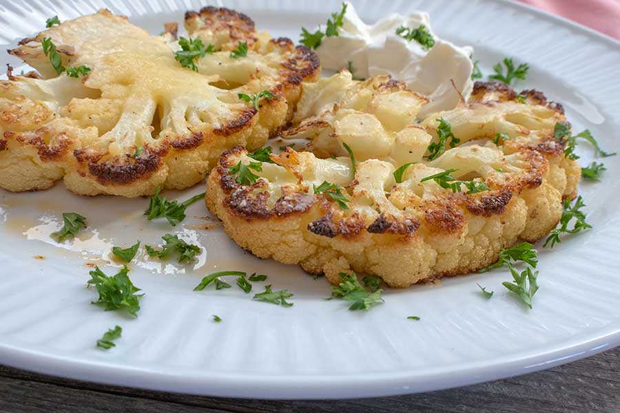 roasted cauliflower steak on a plate with herbs, vegetarian recipe