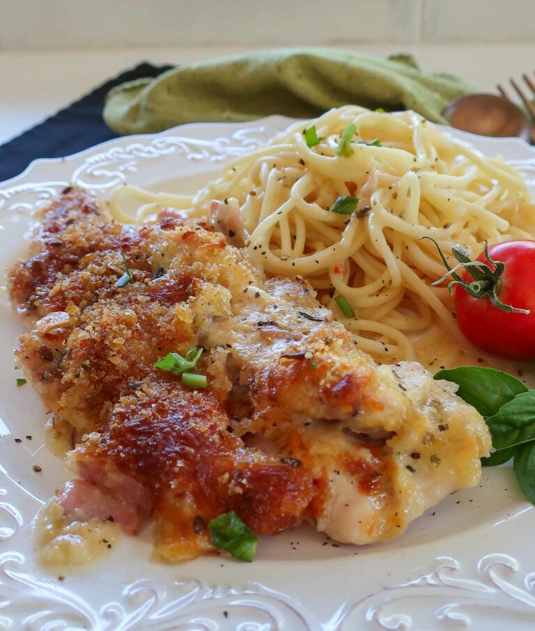 a portion of chicken cordon bleu casserole on a plate with pasta and cream sauce