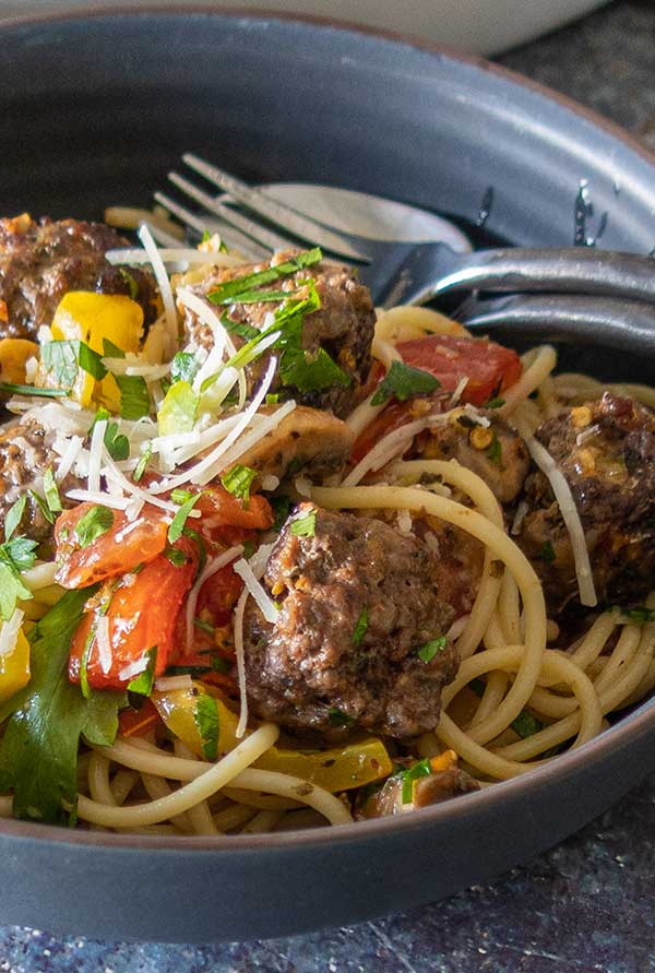 close up of Italian pasta with meatballs, herbs, parmesan and fresh veggies in a black bowl