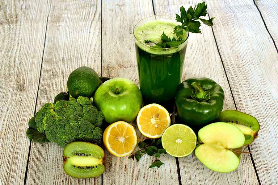 green juice in a glass with lemons, broccoli, kiwi and bell pepper next to it