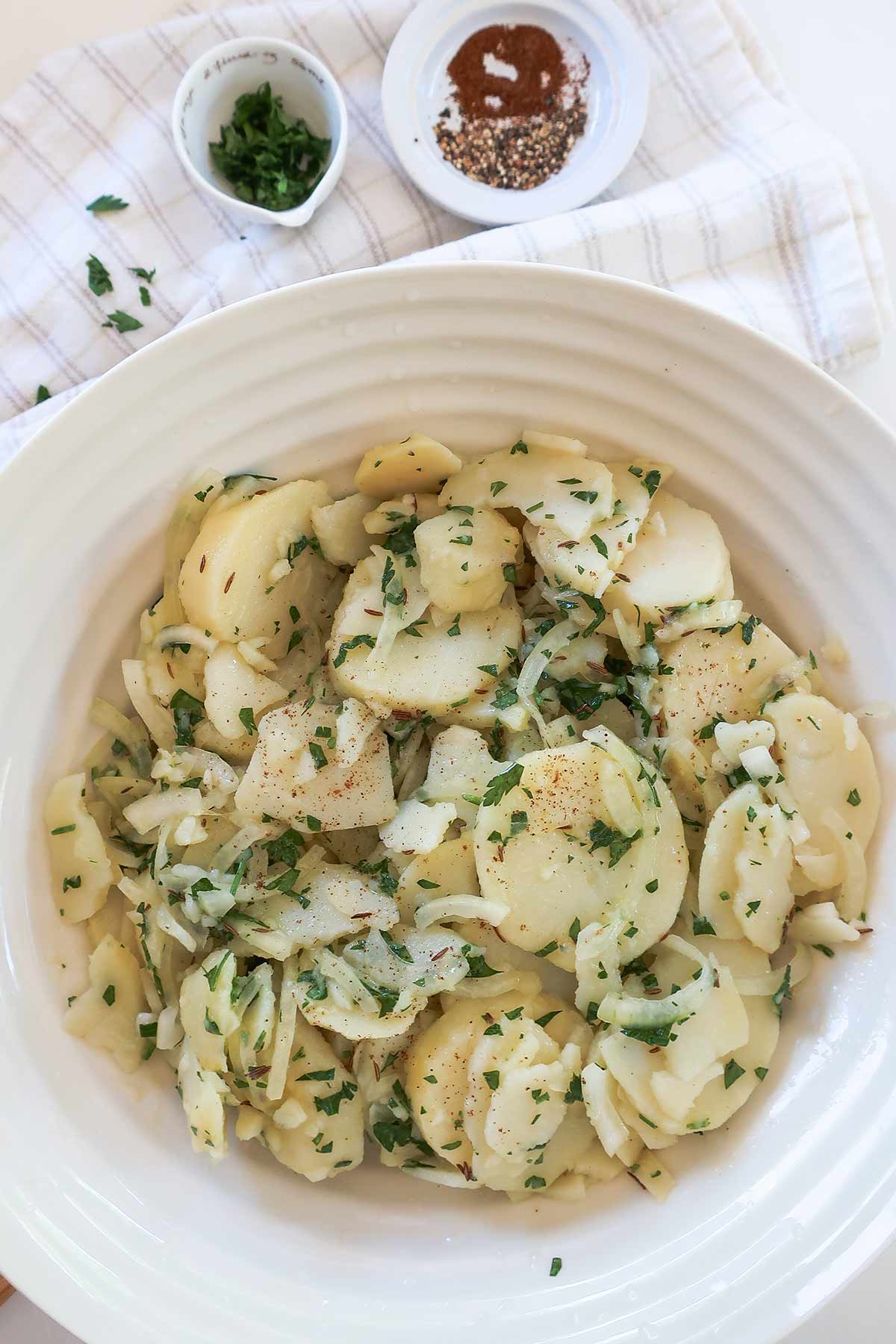 Large salad bowl filled with cooked slice potatoes marinated with vinaigrette, onions and parsley