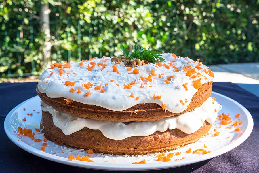 2 layers of carrot cake with cream cheese frosting and carrot gratings on a plate