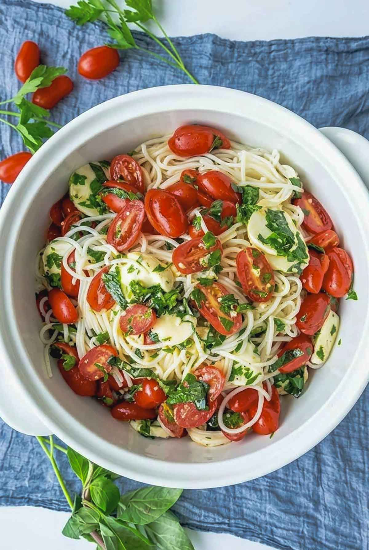 Marinated gluten free Italian pasta salad in a serving bowl with herbs and fresh tomatoes