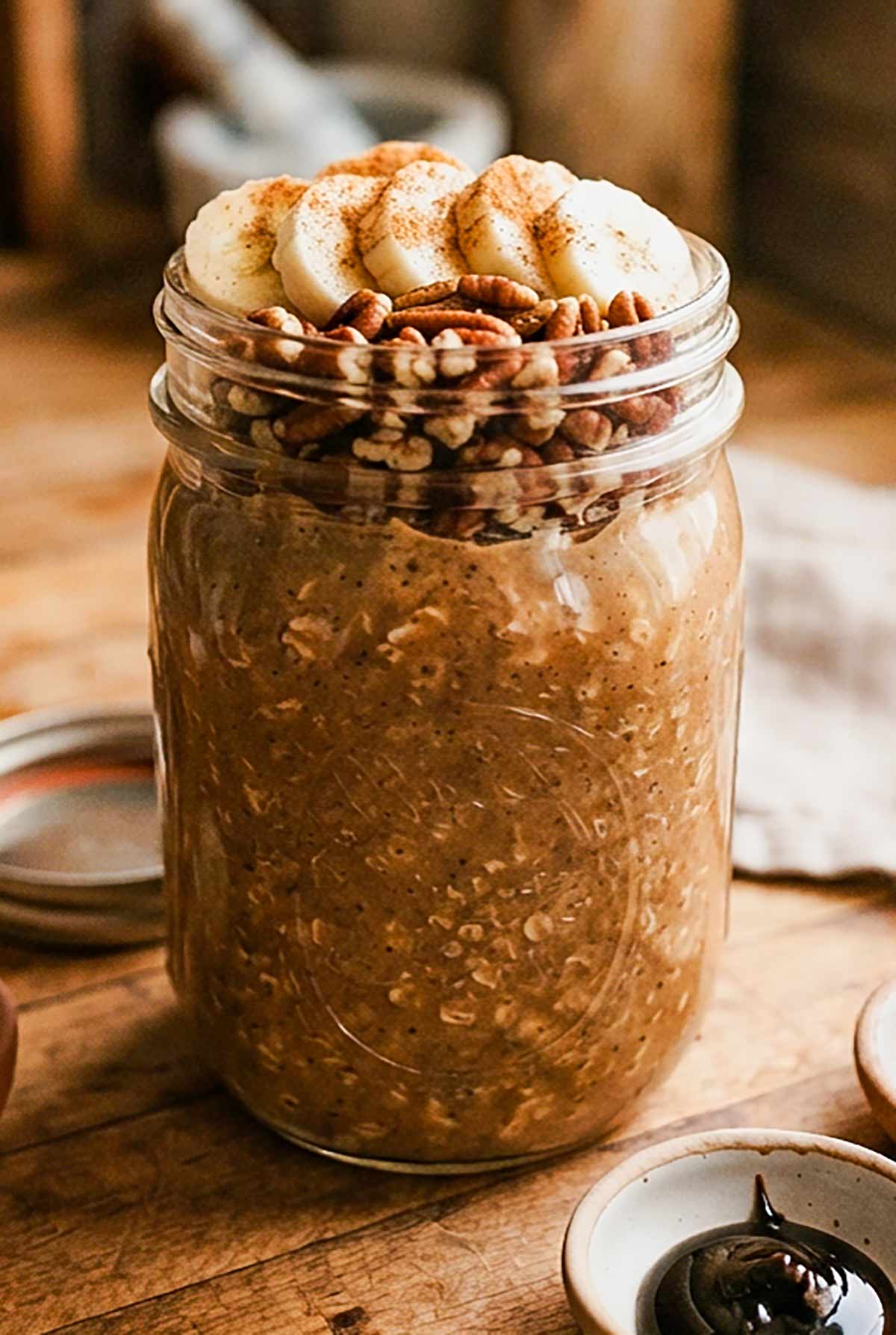a mason jar filled with Gingerbread Overnight Oats with Chia & Hemp Hearts Breakfast and topped with sliced bananas and pecans
