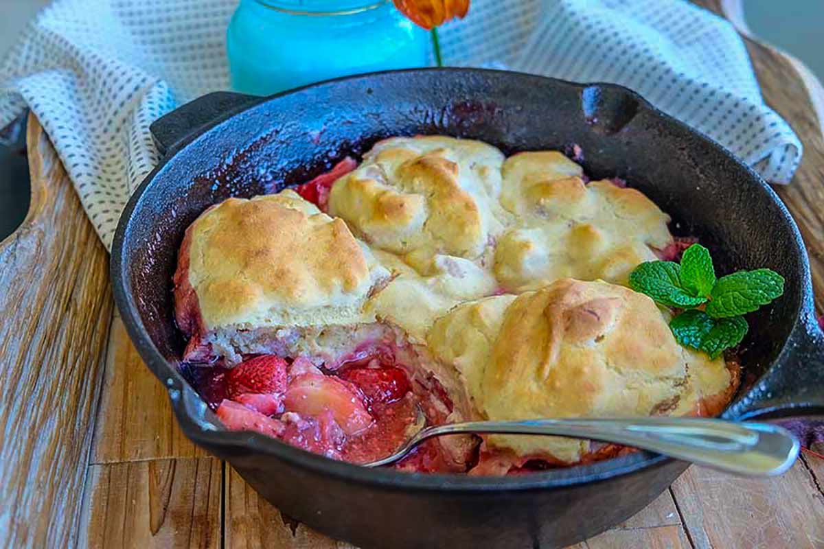 freshly baked gluten free strawberry cobbler in a skillet with cream cheese biscuits