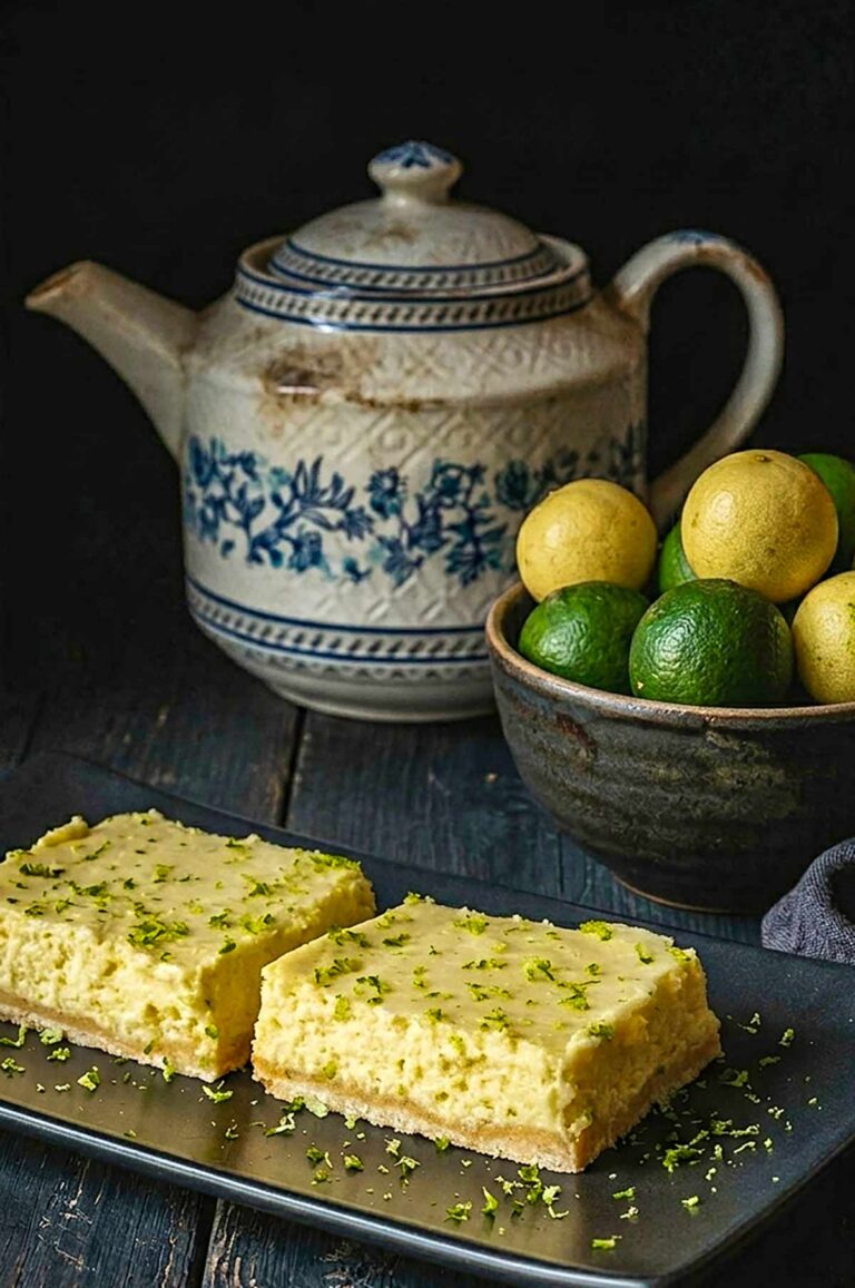 2 Gluten-Free Key Lime Squares on a black plate with key limes in a bowl