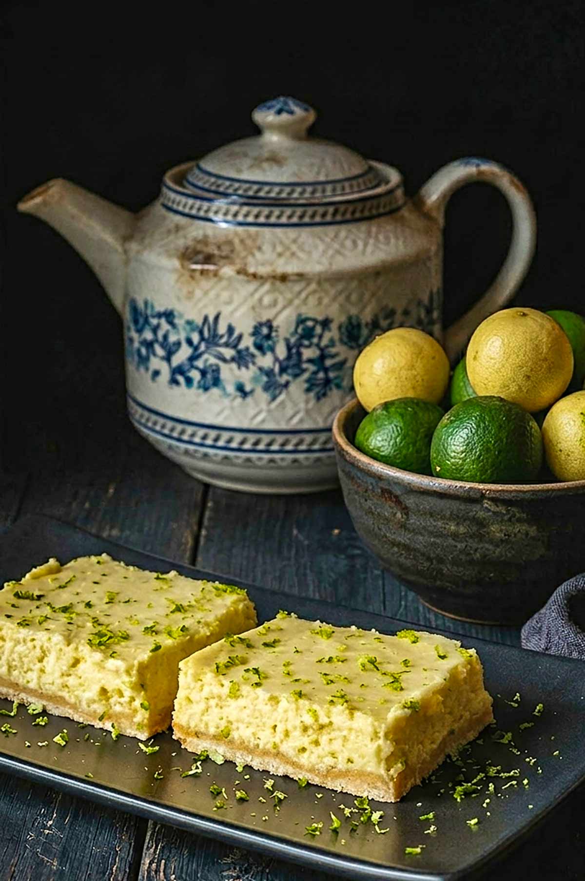 2 Gluten-Free Key Lime Squares on a black plate with key limes in a bowl