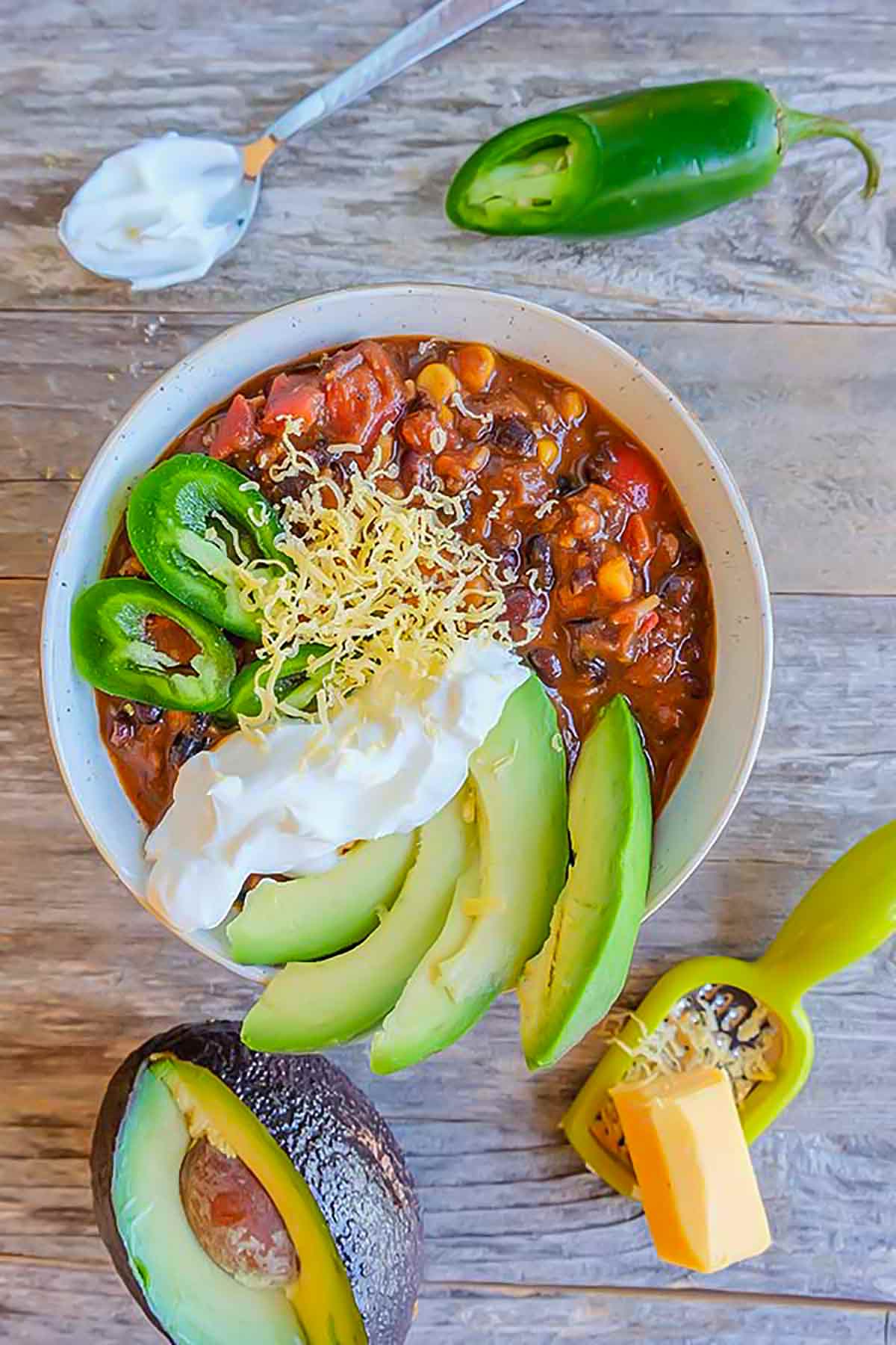 cincinnati black bean chili topped with avocado, sour cream, cheese and jalapeno in a bowl