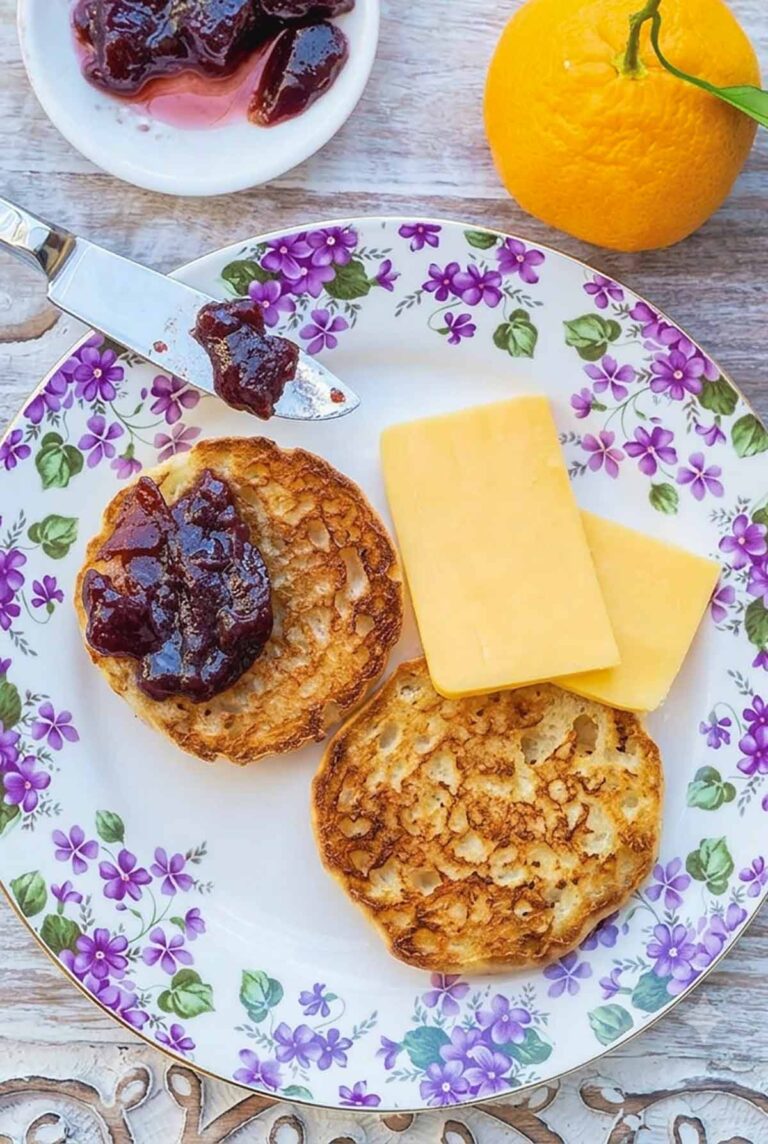 sliced toasted gluten free English muffin topped with jam and a side of cheddar on a plate