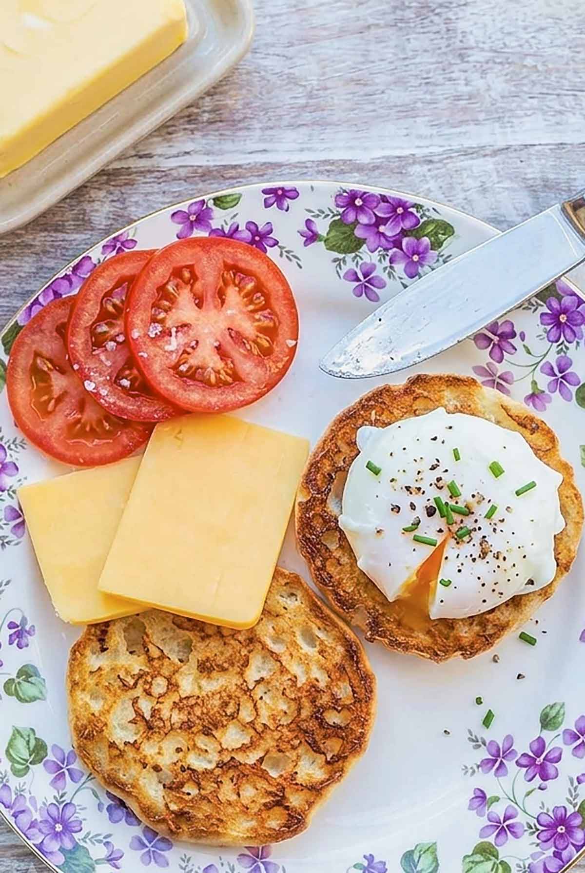 sliced toasted English muffin in half on a plate topped with soft poached egg, sliced tomatoes and cheddar on the side.