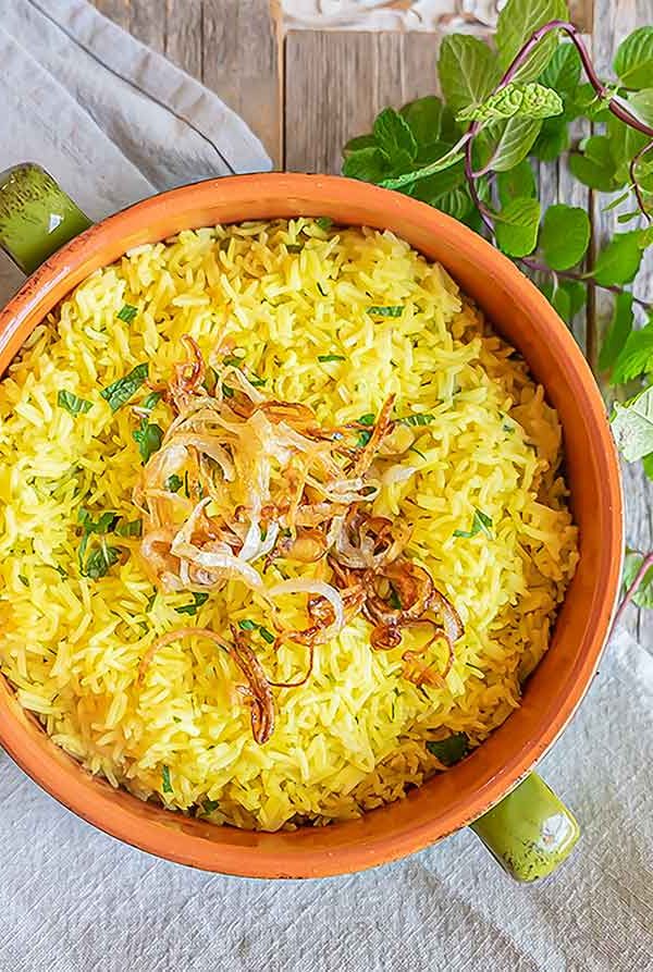 yellow rice with mint in a bowl topped with onions