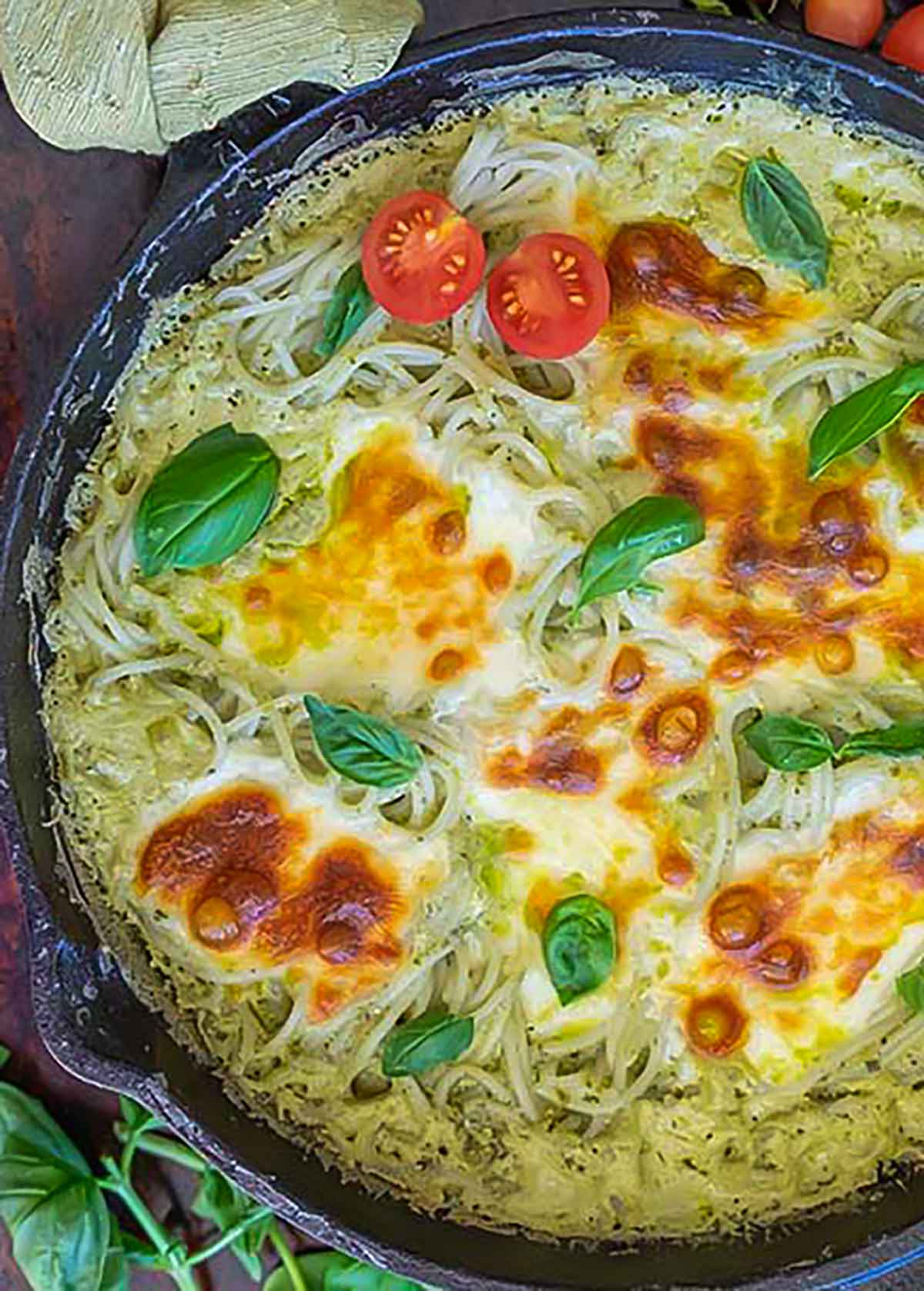 One-pot Alfredo basil pasta bake in a cast iron skillet, topped with melted cheese and halved cherry tomatoes