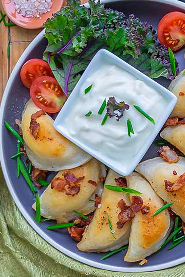 perogies on a plate with sour cream and tomatoes
