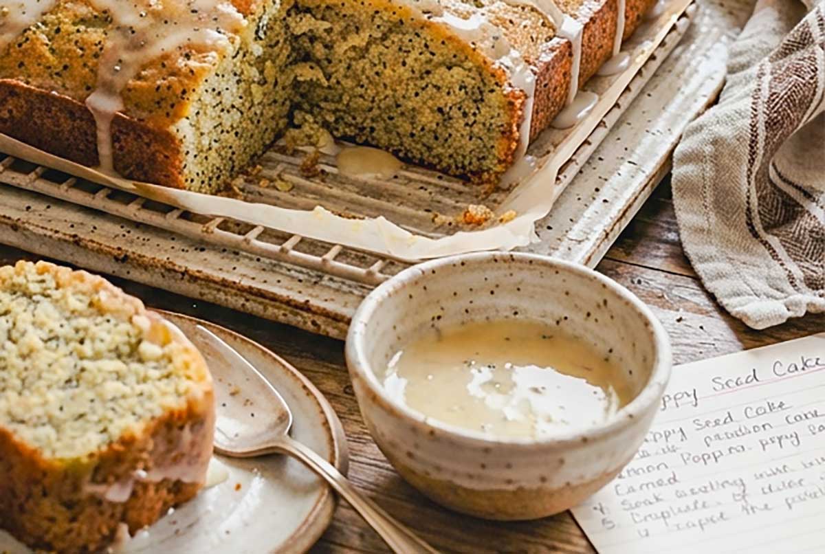 close of up a slice of Gluten-Free Lemon Poppy Seed Cake with a side bowl of lemon glaze