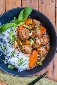 sweet and sour meatballs in a bowl with noodles and fresh basil