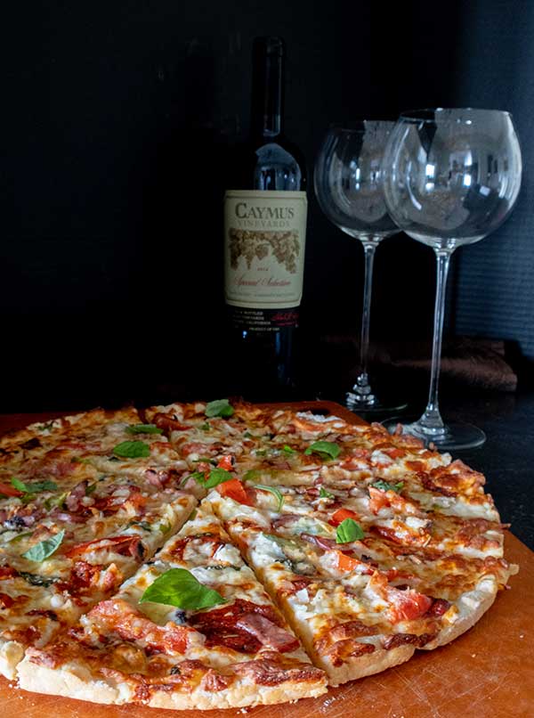 sliced gluten free thin crust pizza with toppings, with wine and wine glasses