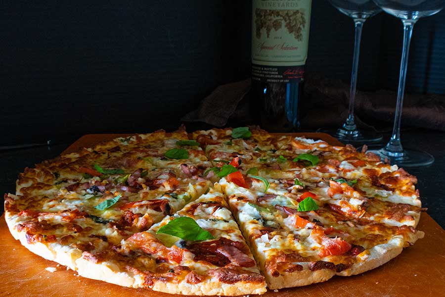 sliced thin crust pizza with a wine bottle and two wine glasses