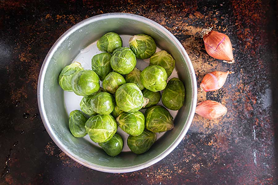 whole brussel sprouts in a bowl with three shallots on the side
