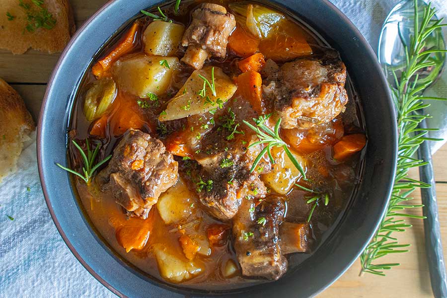 oxtail soup in a bowl with herbs on a tray with a spoon