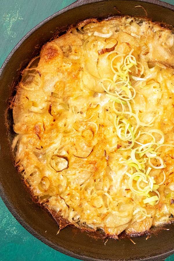 potato gratin topped with leeks in cast iron skillet