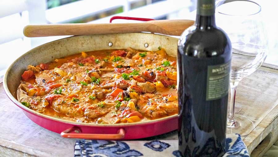 spanish pork and sausage casserole in a skillet with bottle of wine