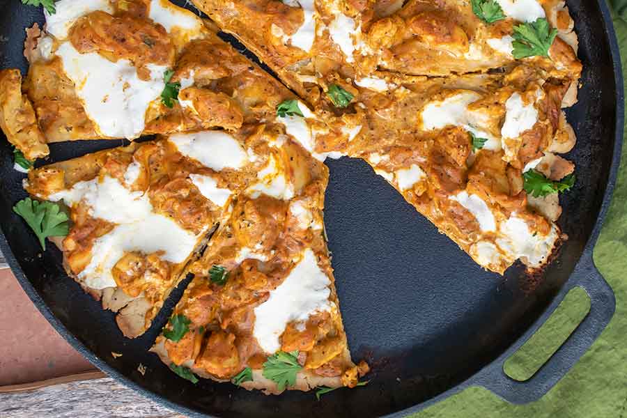 sliced butter chicken pizza on a cast iron skillet