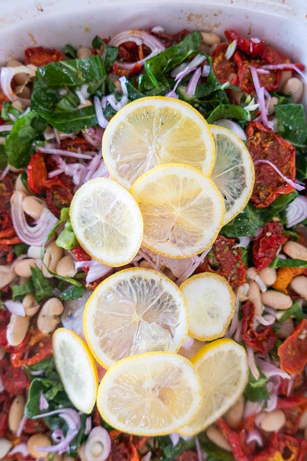 roast fish with cannelloni beans, sun dried tomatoes and greens topped with lemon slices