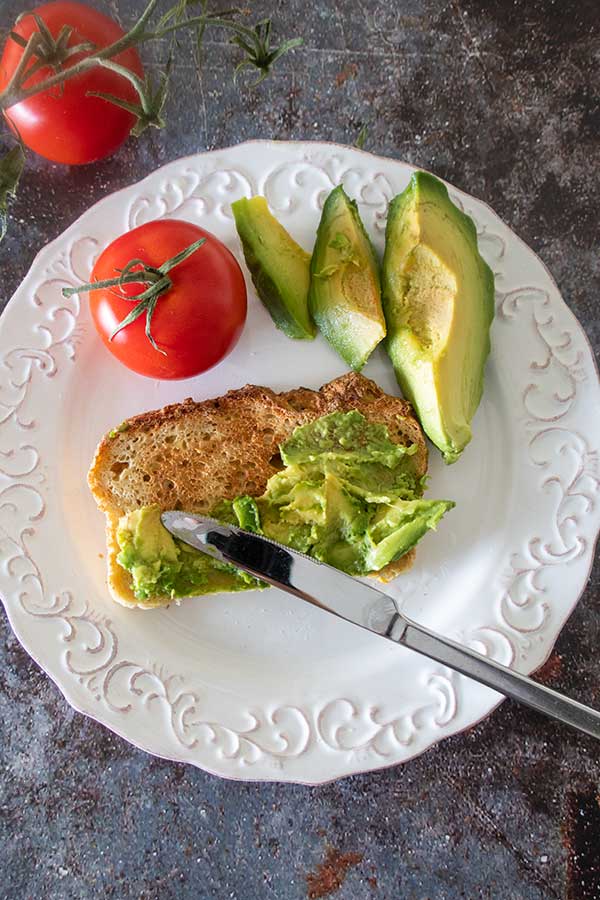 toasted millet bread topped with avocado on a plate with a tomato