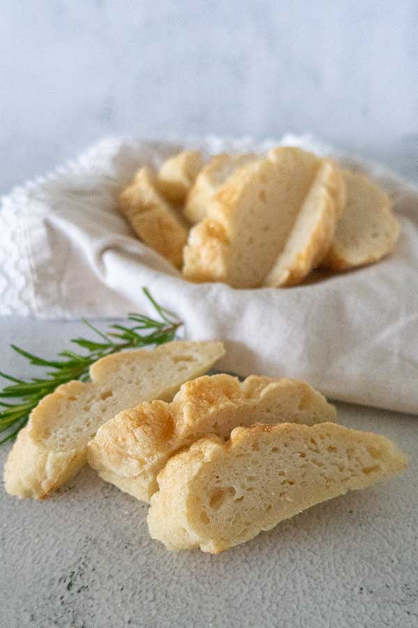 sliced gluten free Italian bread in a basket with a rosemary twig