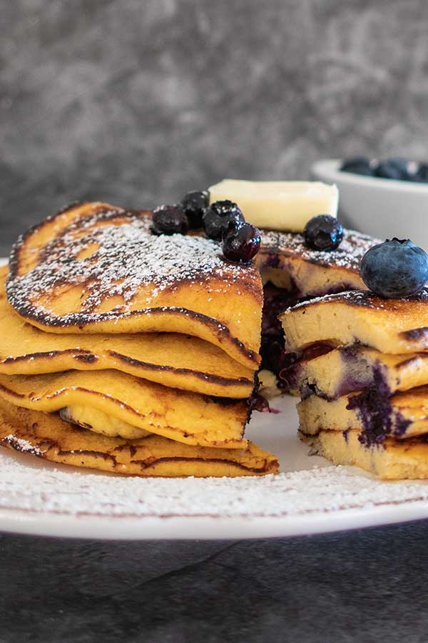stacked coconut flour pancakes on a plate and topped with blueberries