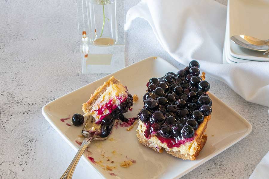 fork cutting a piece of 3 layer blueberry key lime cake on a dessert platter