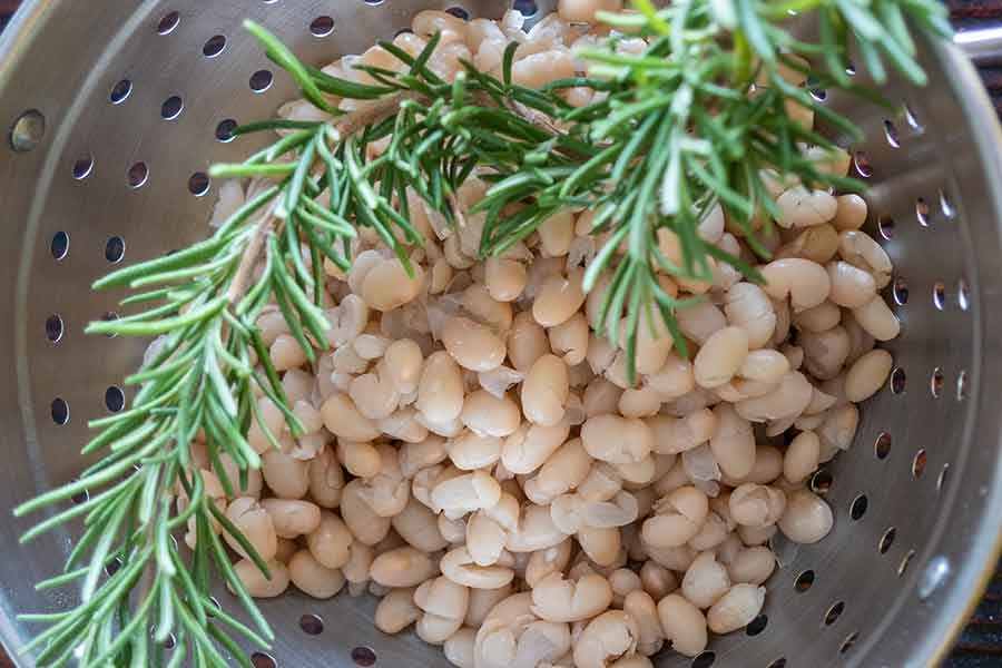 cooked white beans and rosemary in a colander