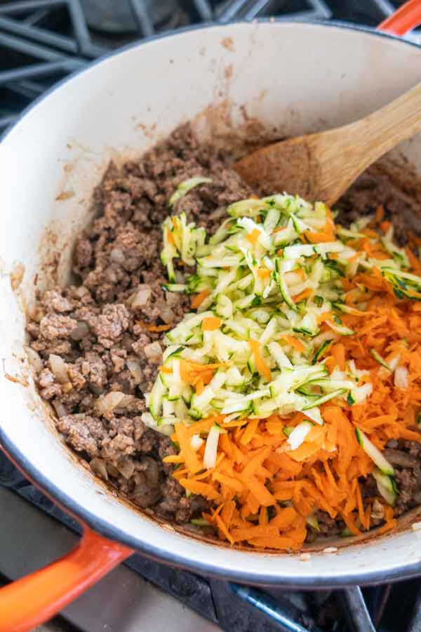 ground beef, grated zucchini and carrots with hamburger helper in a pot
