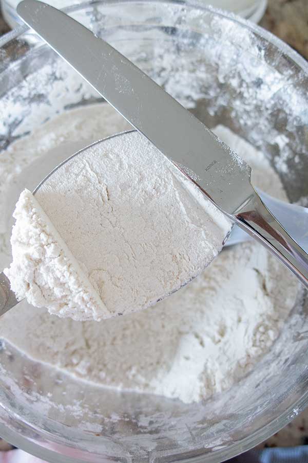 measuring cup filled with flour levelled using a knife