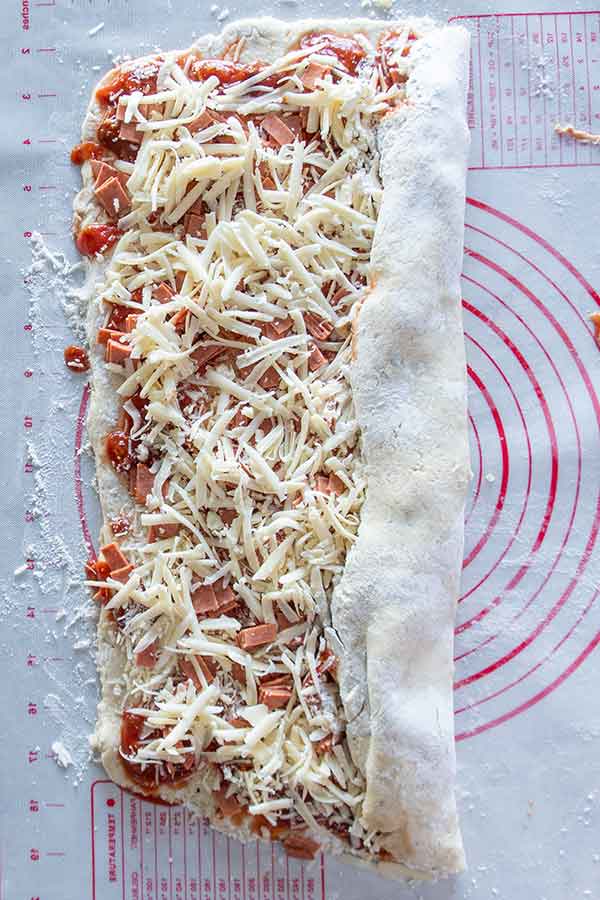 rolling pizza dough with toppings into a log