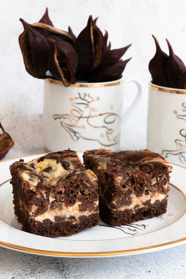 2 brownie squares on a plate with 2 mugs in the background