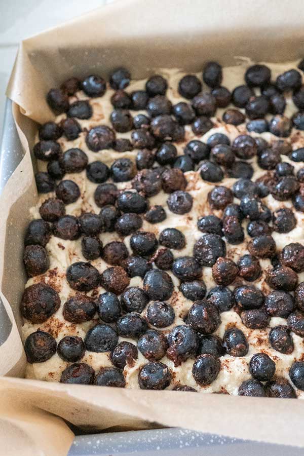 coffee cake batter topped with blueberries in a square pan