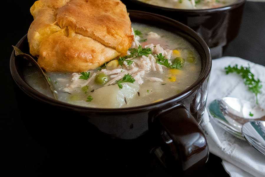 chicken pot pie soup with a roll in a bowl