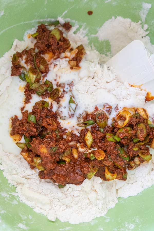 flour mixed with sausage, buttermilk and green onions in a bowl