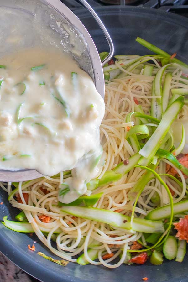 cheese sauce pouring into pasta, salmon, and asparagus 